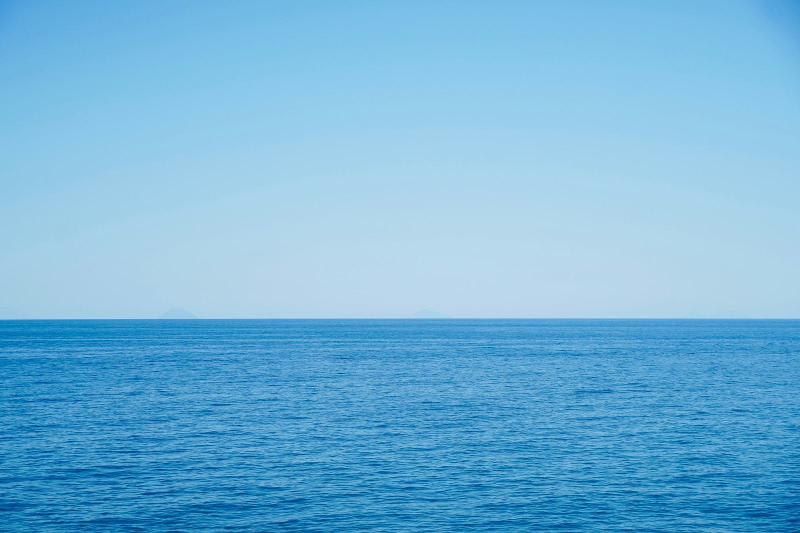 Calm open ocean meeting a clear pale sky at a straight horizon, with gentle ripples and no land in the foreground.